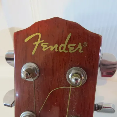Sale Photo Thumbnail #122: Headstock detail of a Fender acoustic guitar featuring gold logo decal, mahogany veneer, and chrome tuning pegs.