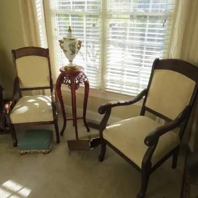 Sale Photo Thumbnail #11: Pair of traditional wooden armchairs with cream upholstered seats and backrest panels, positioned near a window alongside a tall Asian-style plant stand holding an ornate porcelain urn.