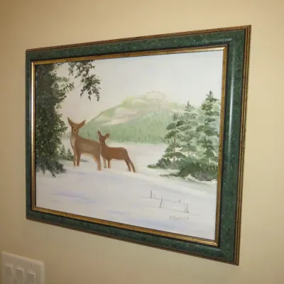 Sale Photo Thumbnail #42: Framed winter landscape painting depicting deer in a snowy forest, signed by the artist in the lower right and set in a green and gold frame.