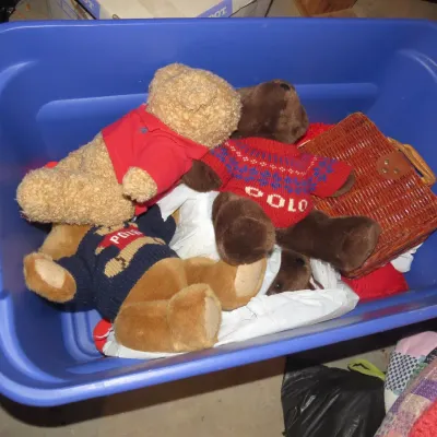Sale Photo Thumbnail #49: Blue plastic storage bin containing plush Polo Ralph Lauren teddy bears wearing branded sweaters and shirts, alongside a small woven wicker basket.