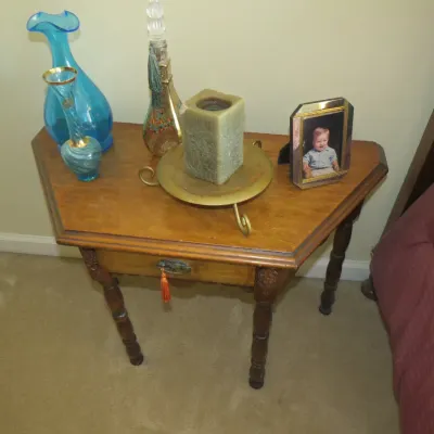 Sale Photo Thumbnail #78: Vintage pentagonal wood side table with turned legs, decorated with turquoise glassware, a brass candle holder, decor, and a framed photo.