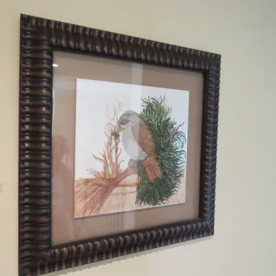 Sale Photo Thumbnail #80: Framed watercolor painting of a bird resting on a branch amidst foliage, presented under glass in a dark textured wooden frame.