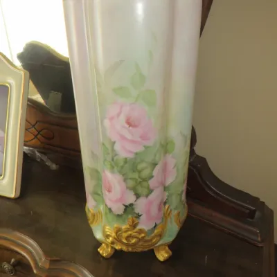 Sale Photo Thumbnail #79: Hand-painted porcelain tall vase featuring soft pink roses, a gold-rimmed top, and ornate gilded scrollwork feet, in an antique Victorian style.