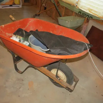 Sale Photo Thumbnail #51: Red plastic wheelbarrow with wooden handles, filled with various gardening supplies and black landscape fabric.