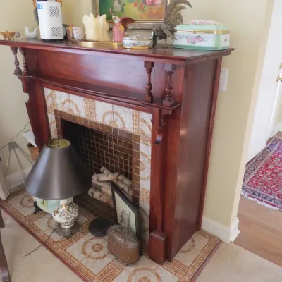 Sale Photo Thumbnail #12: Vintage dark wood mantel surrounds a decorative faux fireplace with fan-patterned tile inlay and small mosaic interior tiles. Features spindle accents and a display shelf topped with assorted decor.