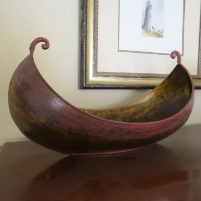 Sale Photo Thumbnail #77: Rustic metal boat-shaped centerpiece bowl with a hand-painted red and gold distressed finish, featuring scrolled ends.