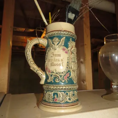 Sale Photo Thumbnail #64: Vintage German ceramic beer stein repurposed as a container for brushes and decor, featuring detailed relief work and German text.