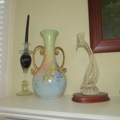 Sale Photo Thumbnail #38: Hand-painted porcelain urn with double gilded handles featuring a floral and grape design, displayed alongside glass tabletop decor.