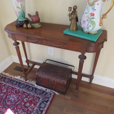Sale Photo Thumbnail #18: Neoclassical style wooden console table featuring carved apron details and turned legs, topped with decorative decor including a floral pitcher, figurines, and a lamp.