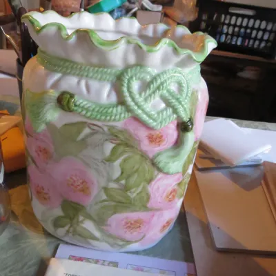 Sale Photo Thumbnail #66: Hand-painted ceramic vase featuring pink floral motifs, ruffled rim, and raised green rope-and-tassel accent.