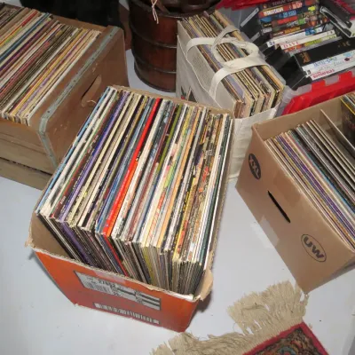 Sale Photo Thumbnail #150: Large collection of vintage vinyl LP records organized in cardboard boxes, wooden crates, and tote bags alongside various DVDs.