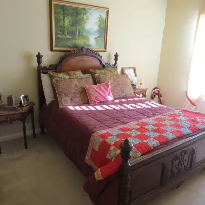Sale Photo Thumbnail #74: Traditional carved dark wood bed frame with intricate scrollwork and turned finials, complemented by a patchwork quilt, bedside table, and framed landscape painting.
