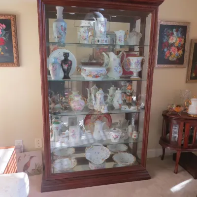 Sale Photo Thumbnail #3: Large wooden curio cabinet with glass shelves and interior lighting, filled with a collection of fine porcelain tea sets, vases, and figurines.
