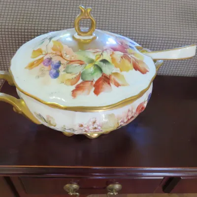 Sale Photo Thumbnail #29: Hand-painted porcelain tureen with matching lid and ladle, featuring gilt trim and a fruit and botanical motif.