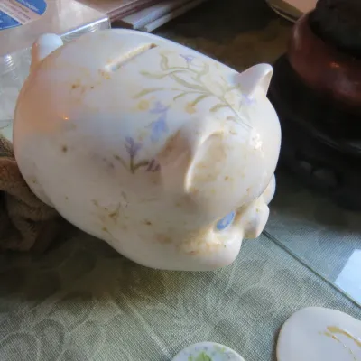Sale Photo Thumbnail #67: Vintage white ceramic piggy bank featuring delicate pastel floral motifs and blue painted eyes.