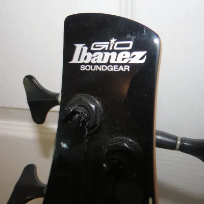 Sale Photo Thumbnail #99: Headstock detail of an Ibanez Gio Soundgear electric bass guitar with a gloss black finish and black tuning pegs.