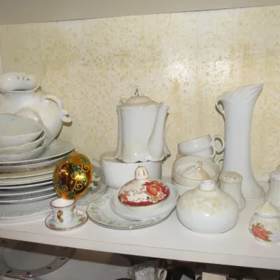 Sale Photo Thumbnail #63: A collection of vintage porcelain tableware and decorative items including a teapot, pitcher, plates, saucers, and salt shakers, displayed on a cabinet shelf.