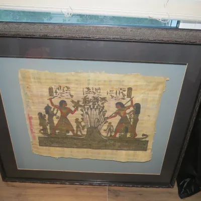 Sale Photo Thumbnail #44: Framed Egyptian papyrus painting depicting figures in a boat surrounded by hieroglyphics, presented in a dark ornate wooden frame with double matting.