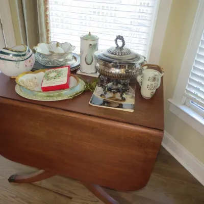 Sale Photo Thumbnail #39: Vintage drop-leaf wooden accent table topped with various decorative tableware, including a silver-plated chafing dish, floral china bowls, porcelain teapot, and small tea cups.