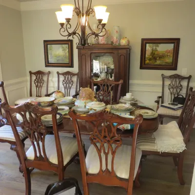 Sale Photo Thumbnail #22: Traditional mahogany dining set featuring a large oval table with carved Chippendale-style chairs and an assortment of vintage china displayed on top.