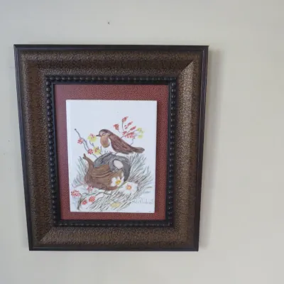 Sale Photo Thumbnail #41: Hand-painted ceramic tile featuring a bird perched on a branch, mounted in a textured brown frame with a red pebbled mat.