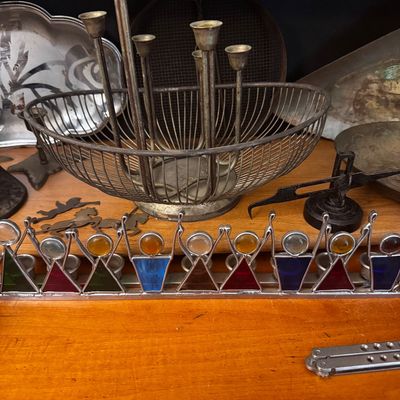 Sale Photo Thumbnail #40: Stained glass and metal dancing figures Hanukkah menorah, displayed alongside a metal centerpiece basket with built-in candle holders and various vintage metal tableware.