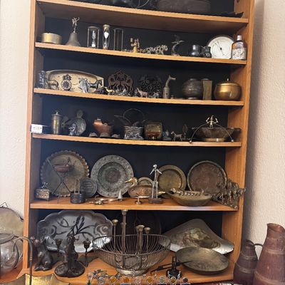 Sale Photo Thumbnail #50: Wooden shelving unit displaying an extensive collection of vintage brass, pewter, and metal decorative items, including trays, figurines, candelabras, and a stained glass menorah.