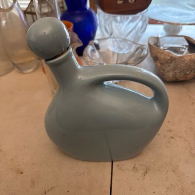 Sale Photo Thumbnail #5: Vintage slate blue ceramic jug decanter with a spherical stopper and integrated handle, displayed among various glassware items.