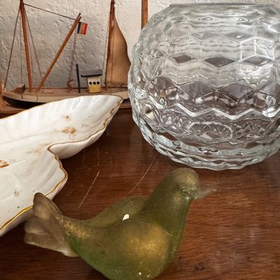 Sale Photo Thumbnail #15: Collection of tabletop decor including a green glass bird figurine, a textured clear glass globe vase, a leaf-shaped ceramic dish, and a framed miniature sailboat model.