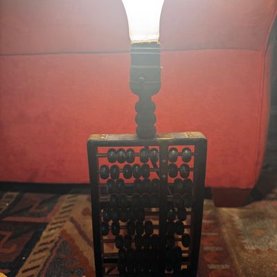 Sale Photo Thumbnail #29: Unique vintage table lamp crafted from a wooden and brass Chinese abacus base, shown lit.
