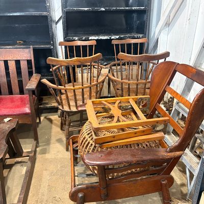 Sale Photo Thumbnail #59: Collection of vintage wooden chairs including captain's chairs, a ladder-back armchair, and an Arts and Crafts style chair alongside metal shelving units.