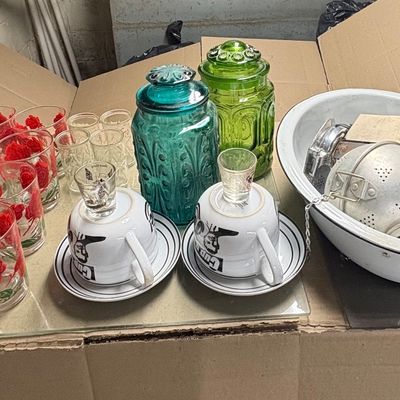 Sale Photo Thumbnail #95: Collection of vintage household items including red floral drinking glasses, blue and green Moon and Stars glass canisters, teacups with saucers, and an enamel basin filled with kitchen gadgets.