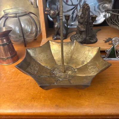 Sale Photo Thumbnail #27: Vintage brass umbrella-shaped catchall dish featuring etched ornate detailing and a hook handle, displayed alongside copper and silver decorative items.