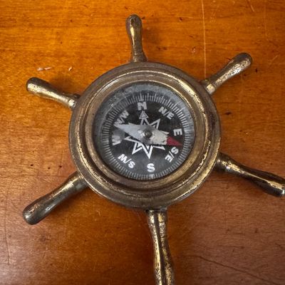 Sale Photo Thumbnail #47: Vintage brass ship's wheel pocket compass with aged patina resting on a wooden surface.