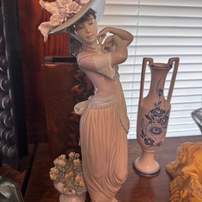 Sale Photo Thumbnail #38: Lladró style porcelain figurine of an elegant woman wearing a floral wide-brim hat and pink gown, shown alongside decorative vases.