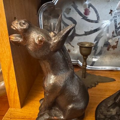 Sale Photo Thumbnail #41: Vintage dark bronze or cast iron braying donkey figurine sitting on a wooden shelf alongside a brass candlestick and silver-toned tray.