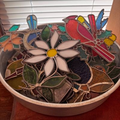 Sale Photo Thumbnail #18: Collection of handcrafted stained glass suncatchers in a metal tray, featuring designs such as a cardinal, daisy, and bluebird.
