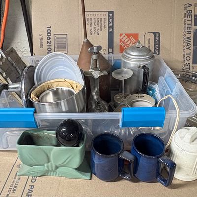 Sale Photo Thumbnail #92: Clear plastic storage tote filled with assorted vintage kitchenware, including a percolator, cast iron waffle iron, pottery mugs, and glass cookware.