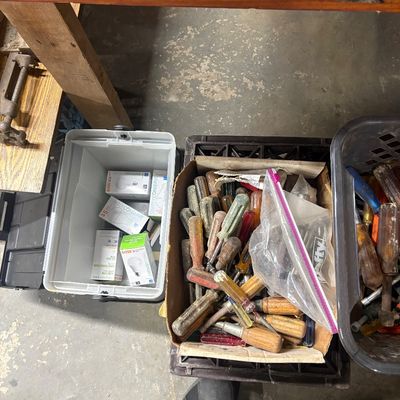 Sale Photo Thumbnail #75: Collection of vintage hand tools including a cardboard box filled with assorted screwdrivers alongside LED lightbulb boxes stored in a plastic bin.