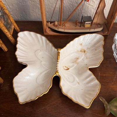 Sale Photo Thumbnail #14: Vintage white ceramic butterfly-shaped trinket dish with gold rim accents, displaying minor surface staining, set alongside a framed shadowbox model boat.