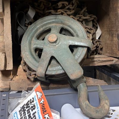 Sale Photo Thumbnail #61: Vintage heavy-duty industrial chain hoist with a cast iron pulley wheel and large lifting hook, showing signs of age and surface rust.