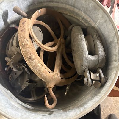 Sale Photo Thumbnail #68: Galvanized metal tub filled with vintage farm equipment and hardware, including cast iron pulleys, a wooden block and tackle, and hooks.