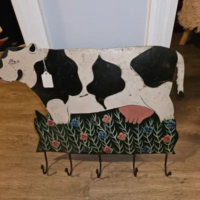 Sale Photo Thumbnail #17: Folk art style painted metal cow wall rack featuring five lower hanging hooks and a floral grass detail along the bottom.