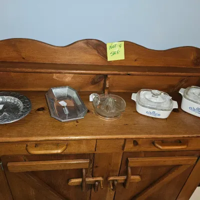 Sale Photo Thumbnail #62: Selection of vintage kitchenware including CorningWare blue cornflower casserole dishes, a glass citrus juicer, and metal serving trays, displayed on a wooden hutch marked not for sale.
