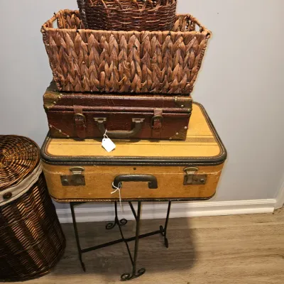 Sale Photo Thumbnail #33: Stack of vintage decorative luggage cases and woven baskets displayed on a small wrought iron stand, accompanied by a tall dark wicker hamper.