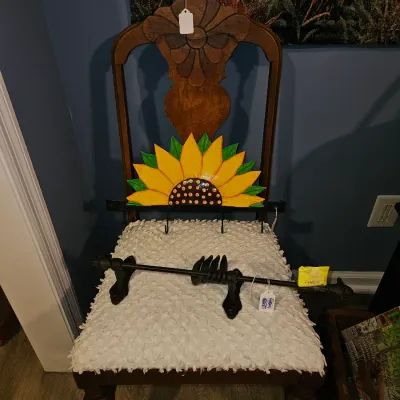 Sale Photo Thumbnail #59: Vintage carved wooden chair with textured white upholstery, featuring a painted sunflower wall rack and a wrought iron fixture resting on the seat.