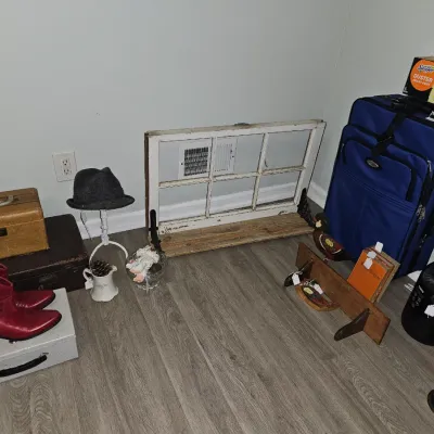 Sale Photo Thumbnail #46: An assortment of floor items including vintage luggage, red cowboy boots, a rustic window frame, blue upright suitcase, and small decorative accessories.
