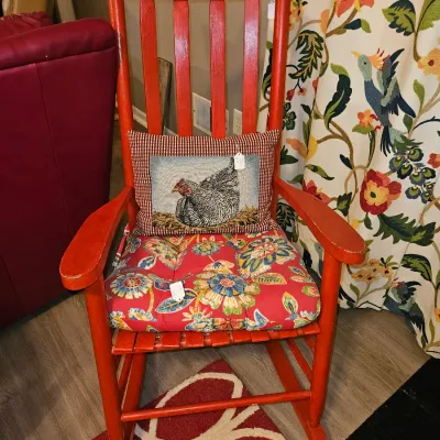 Sale Photo Thumbnail #34: Red painted wooden slat-back rocking chair featuring a floral seat cushion and a needlepoint chicken throw pillow.