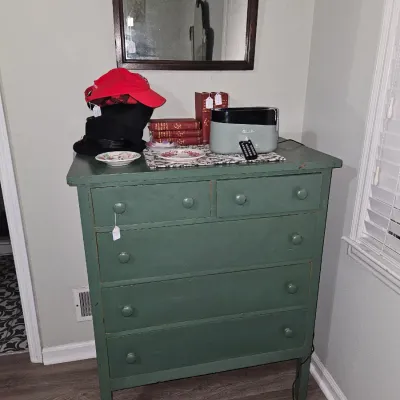 Sale Photo Thumbnail #21: Vintage green painted wooden chest of drawers topped with a mirror, small electronics, decor, and hats.