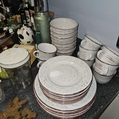 Sale Photo Thumbnail #42: Rustic white ceramic dinnerware set featuring red rim detail with matching bowls and teacups, shown alongside a vintage Stanley thermos.
